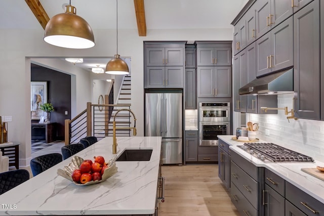 kitchen with stainless steel appliances, under cabinet range hood, beamed ceiling, light wood-style floors, and backsplash
