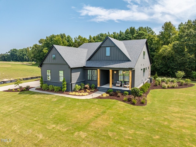 modern inspired farmhouse with board and batten siding, covered porch, a front lawn, a shingled roof, and cooling unit