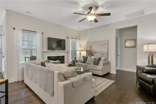 living room with a ceiling fan, dark wood-style floors, baseboards, and a glass covered fireplace