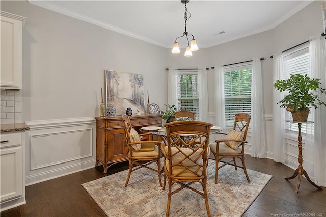 dining area featuring dark wood finished floors, crown molding, a wainscoted wall, and a chandelier