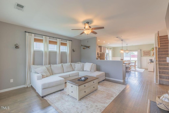 living room with stairs, light wood-style floors, baseboards, a ceiling fan, and a chandelier