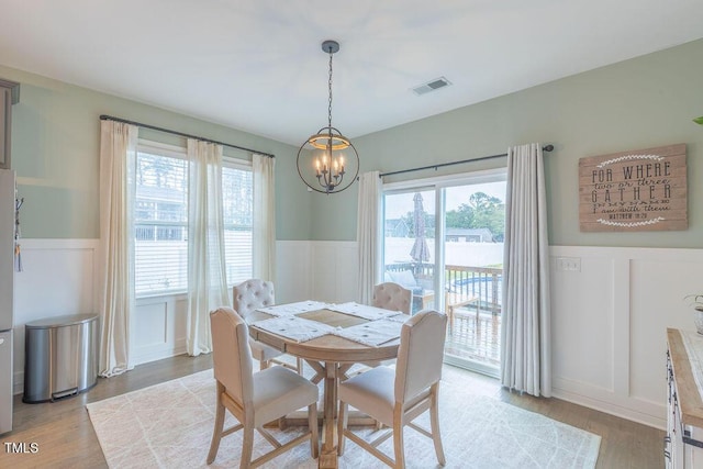 dining area with a decorative wall, wainscoting, a chandelier, plenty of natural light, and light wood-type flooring