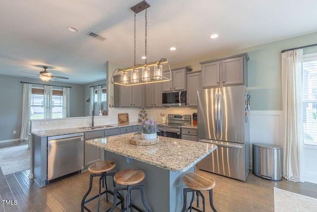 kitchen with stainless steel appliances, gray cabinetry, a sink, wood finished floors, and decorative backsplash