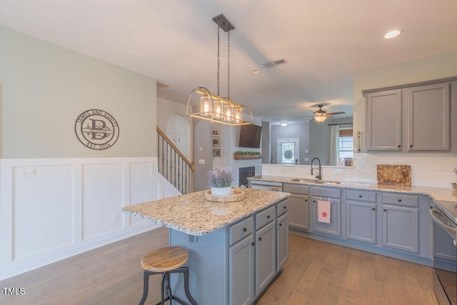 kitchen featuring a sink, gray cabinetry, wood finished floors, ceiling fan, and a wainscoted wall
