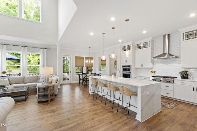 1928 Vandiver Way, Apex, NC 27523 - kitchen featuring wall chimney range hood, appliances with stainless steel finishes, a kitchen breakfast bar, light wood finished floors, and an island with sink