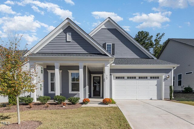 view of front of home with an attached garage, driveway, a porch, a front yard, and a shingled roof