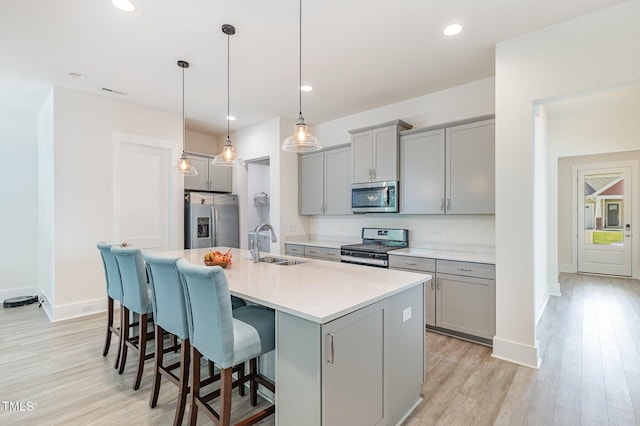 kitchen featuring stainless steel appliances, gray cabinets, a sink, a kitchen island with sink, and light wood-style flooring