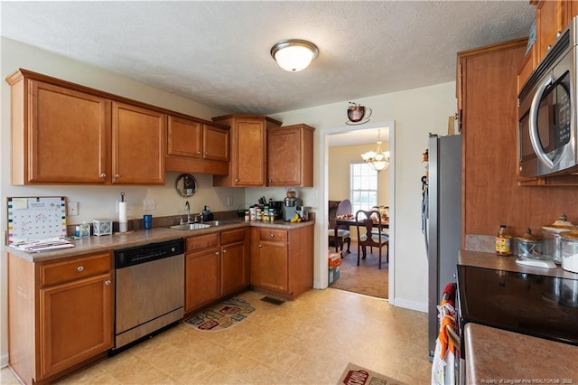 9012 Grouse Run Ln, Fayetteville, NC 28314 - kitchen with appliances with stainless steel finishes, a sink, brown cabinetry, a chandelier, and a textured ceiling