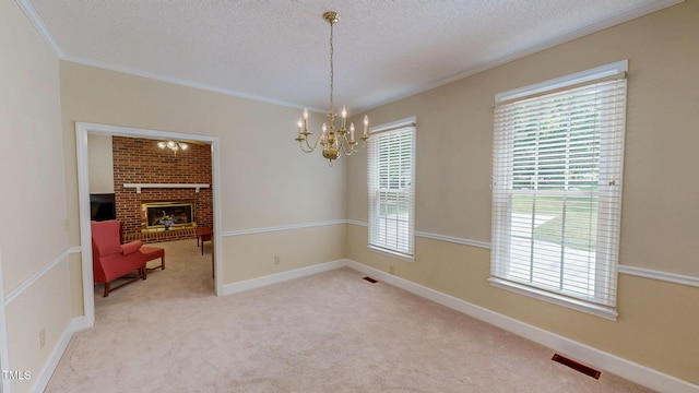 empty room with ornamental molding, a textured ceiling, a chandelier, light carpet, and a brick fireplace