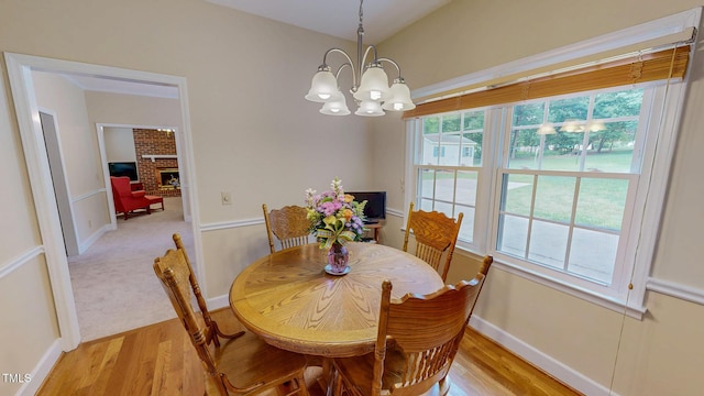 dining space featuring light wood-style flooring, a chandelier, baseboards, a brick fireplace, and vaulted ceiling