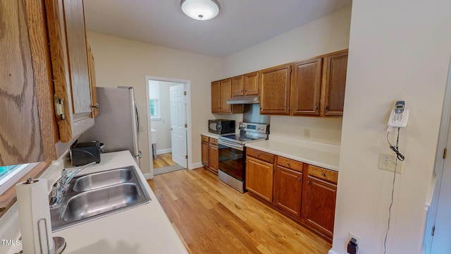 kitchen with appliances with stainless steel finishes, a sink, under cabinet range hood, and light countertops