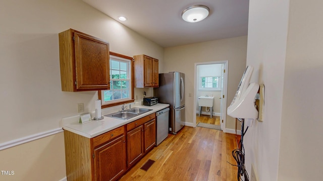 kitchen featuring appliances with stainless steel finishes, a sink, light countertops, light wood-type flooring, and baseboards