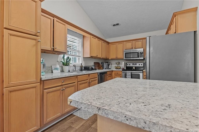 kitchen featuring appliances with stainless steel finishes, lofted ceiling, light wood-type flooring, light countertops, and a sink
