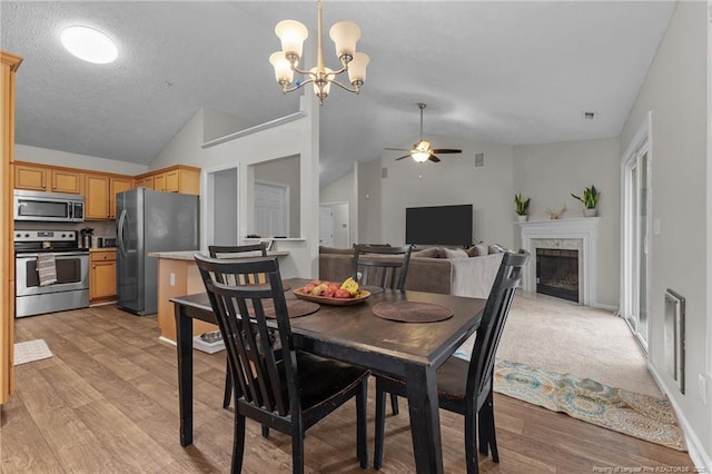dining space with vaulted ceiling, ceiling fan, a chandelier, light wood finished floors, and a fireplace