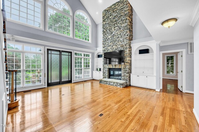 608 Greyrock Rd, Whitsett, NC 27377 - unfurnished living room featuring light wood finished floors, high vaulted ceiling, a stone fireplace, built in shelves, and crown molding