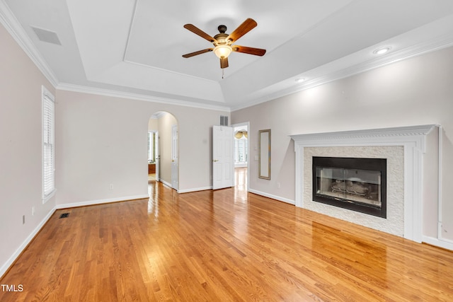 608 Greyrock Rd, Whitsett, NC 27377 - unfurnished living room featuring a raised ceiling, arched walkways, a ceiling fan, a glass covered fireplace, and light wood-style floors