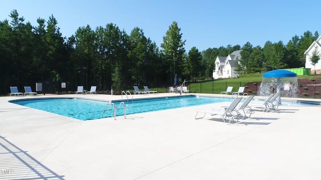 community pool featuring fence, a patio, and view of scattered trees