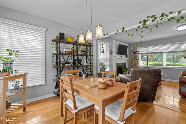 dining space with baseboards, light wood-type flooring, and a glass covered fireplace