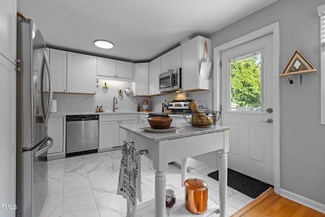 kitchen with stainless steel appliances, a sink, white cabinets, light countertops, and backsplash