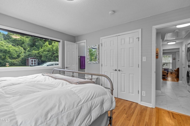 bedroom featuring stacked washing machine and dryer, baseboards, a textured ceiling, multiple windows, and a closet