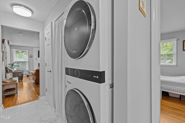 laundry area featuring stacked washer / dryer, light marble finish floors, plenty of natural light, and a textured ceiling