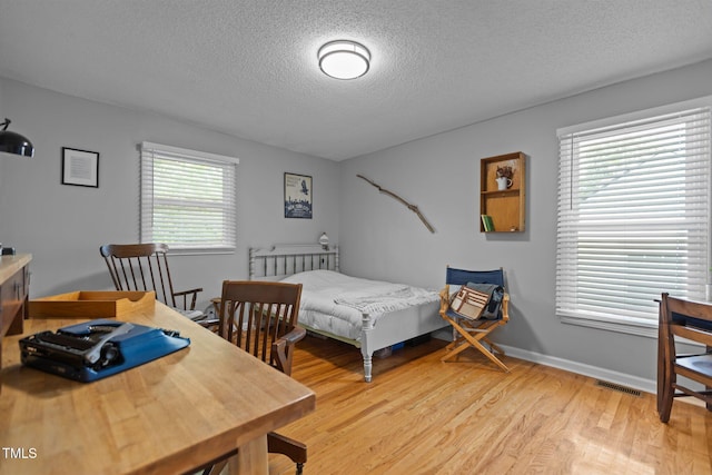 bedroom featuring a textured ceiling, multiple windows, light wood finished floors, and baseboards
