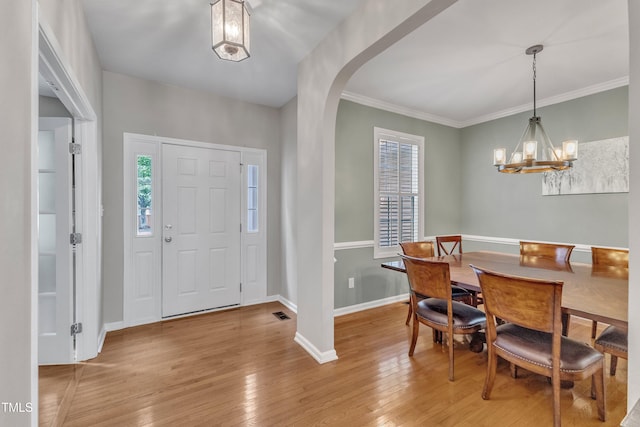 entrance foyer featuring wood-type flooring, plenty of natural light, a chandelier, arched walkways, and ornamental molding