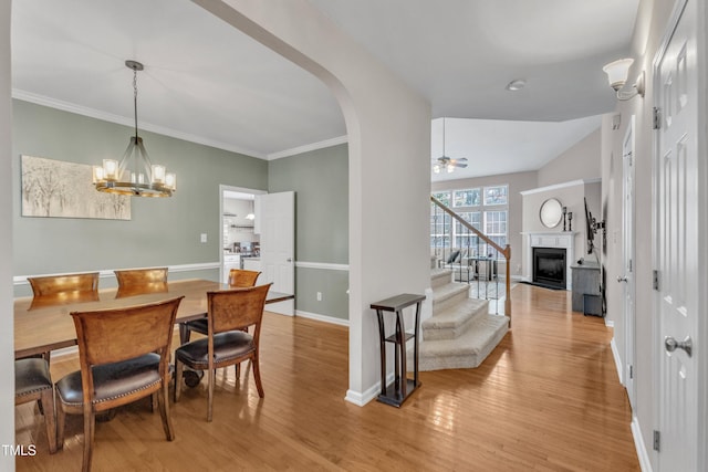dining room featuring stairway, light wood-style floors, a fireplace, baseboards, and a ceiling fan