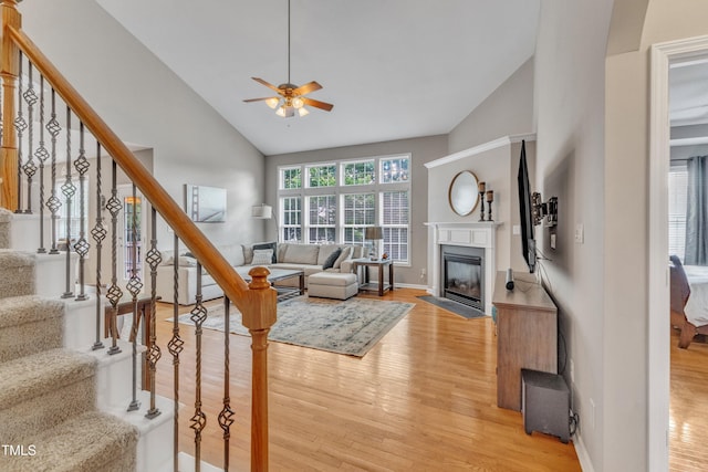 living area with light wood-style floors, a ceiling fan, stairs, and high vaulted ceiling