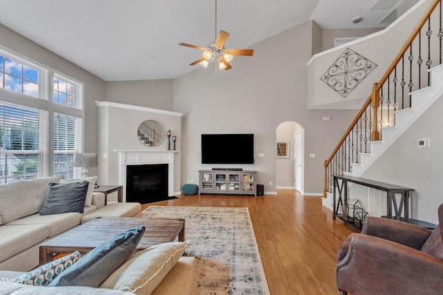 living area with high vaulted ceiling, arched walkways, ceiling fan, stairs, and wood finished floors