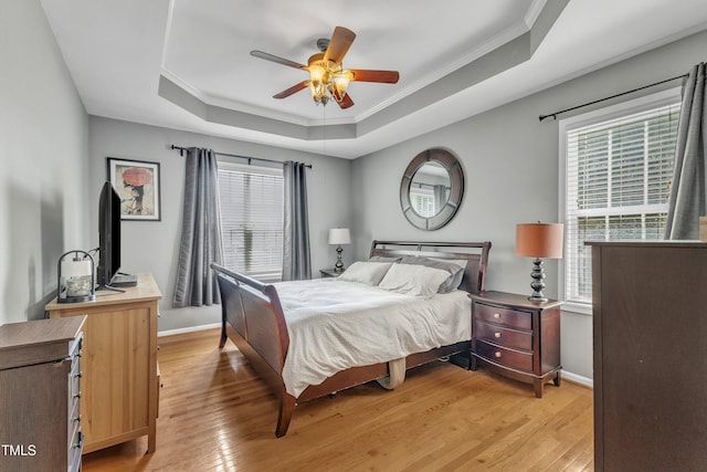 bedroom with a tray ceiling, multiple windows, light wood-style floors, ornamental molding, and baseboards