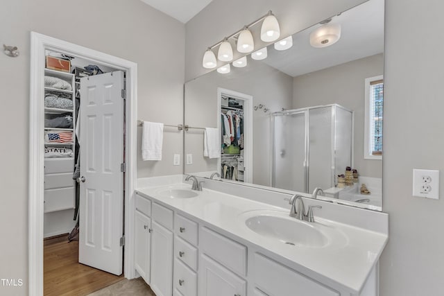 full bath featuring a shower stall, double vanity, a spacious closet, and wood finished floors