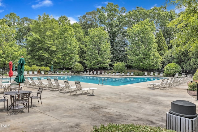 community pool featuring fence, a patio area, and view of wooded area