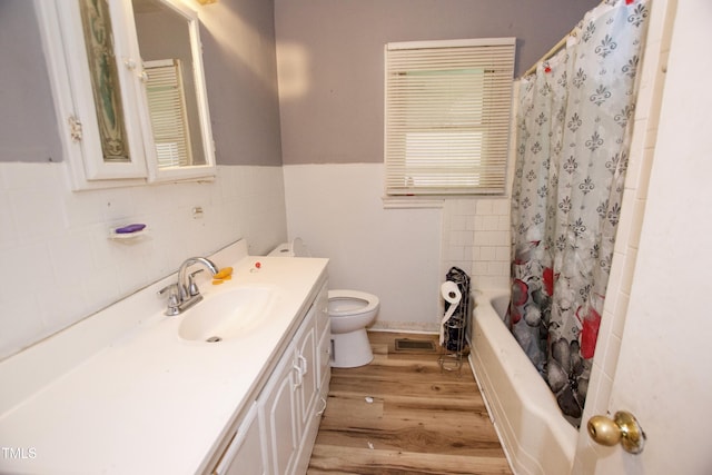 bathroom featuring tile walls, wood finished floors, toilet, vanity, and a wainscoted wall