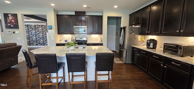 kitchen featuring stainless steel appliances, light stone countertops, tasteful backsplash, a breakfast bar, and dark wood finished floors