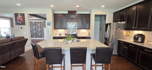 kitchen featuring appliances with stainless steel finishes, a kitchen breakfast bar, light stone countertops, open floor plan, and recessed lighting