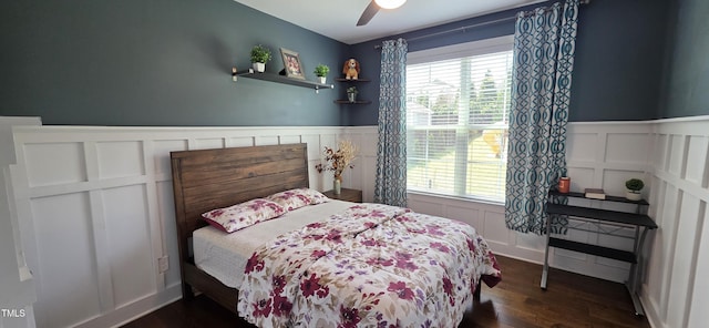 bedroom featuring a decorative wall, wainscoting, dark wood-style floors, and a ceiling fan