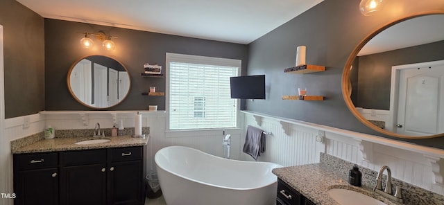 full bathroom with a wainscoted wall, a soaking tub, two vanities, and a decorative wall