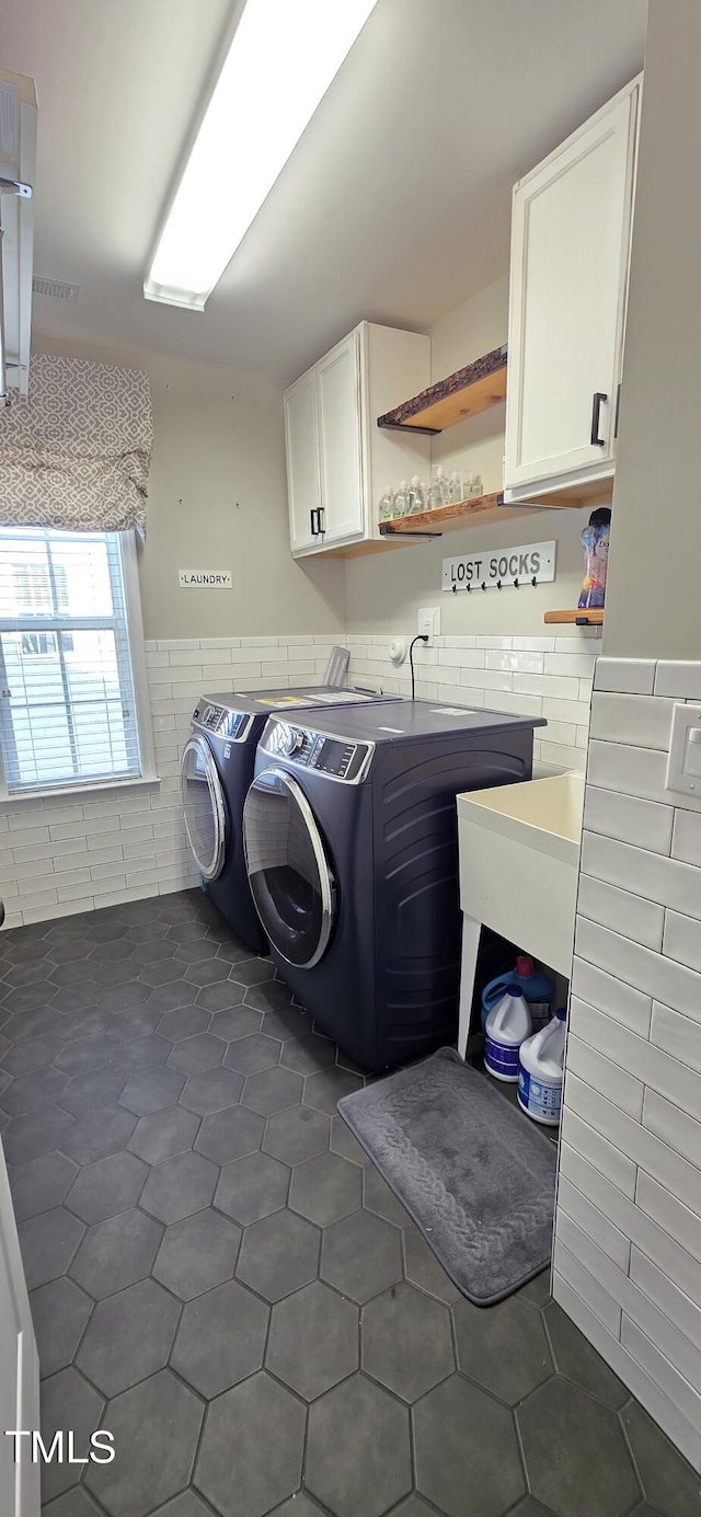 laundry area featuring tile walls, cabinet space, washer and dryer, a wainscoted wall, and dark tile patterned floors