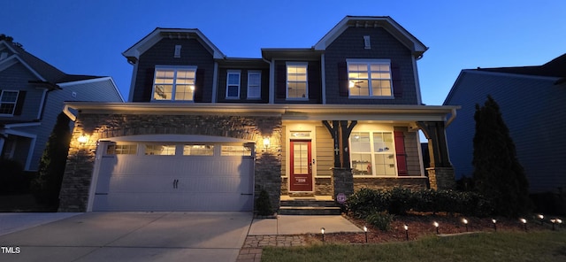 craftsman-style home featuring driveway, covered porch, stone siding, and an attached garage
