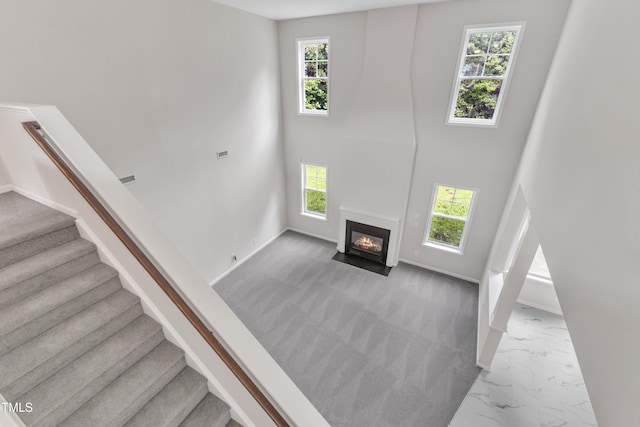 5025 Stonewood Pines Dr, Knightdale, NC 27545 - unfurnished living room featuring plenty of natural light, marble look tiles, stairway, a fireplace with flush hearth, and a high ceiling