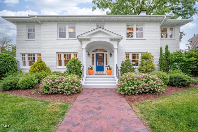 view of front of property with brick siding, a chimney, and a front lawn