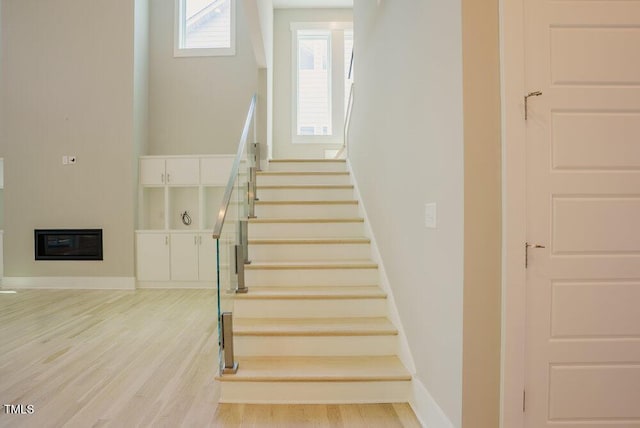 stairs featuring wood finished floors, a glass covered fireplace, and baseboards
