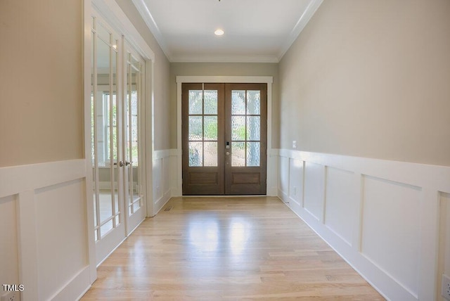 doorway to outside featuring french doors, a decorative wall, a wainscoted wall, crown molding, and light wood finished floors