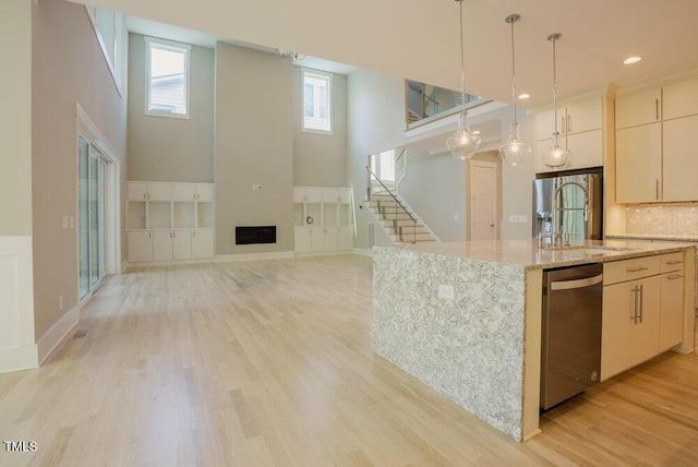 kitchen with appliances with stainless steel finishes, a high ceiling, light wood finished floors, hanging light fixtures, and light stone counters