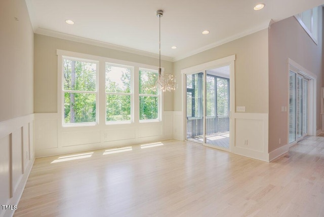 unfurnished dining area with a decorative wall, ornamental molding, light wood-type flooring, a wainscoted wall, and a chandelier