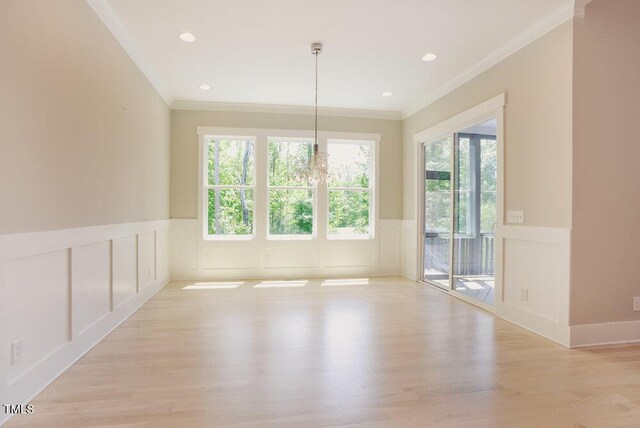 unfurnished dining area with a decorative wall, ornamental molding, healthy amount of natural light, wainscoting, and light wood finished floors