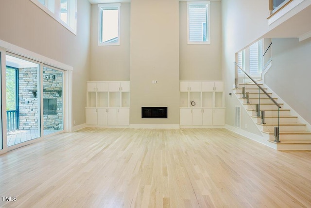 unfurnished living room with a towering ceiling, light wood finished floors, a fireplace, stairway, and baseboards