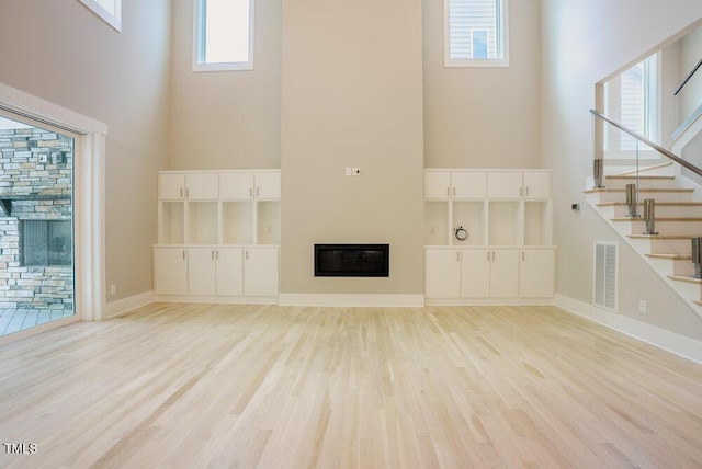 unfurnished living room featuring a glass covered fireplace, a high ceiling, light wood-style flooring, stairs, and baseboards