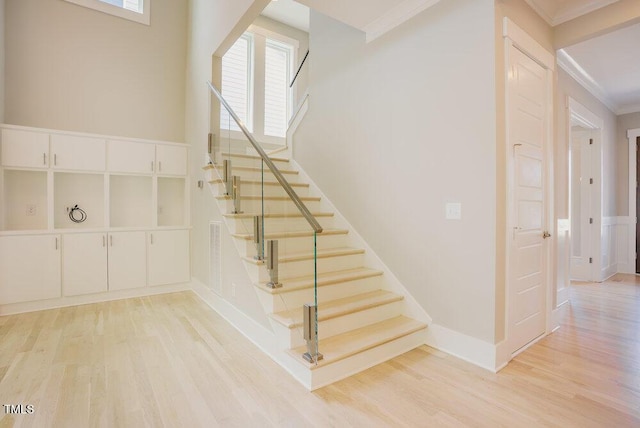 staircase with wood finished floors, ornamental molding, and baseboards